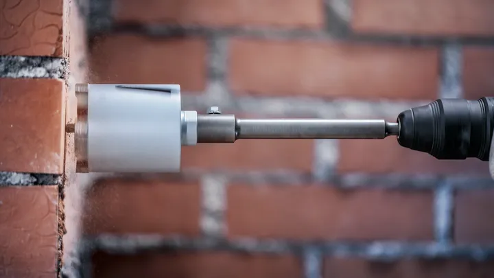Een kernboor maakt een cirkelvormig gat in een rode bakstenen muur.