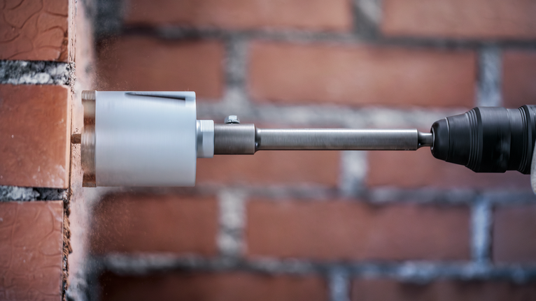 Een kernboor maakt een cirkelvormig gat in een rode bakstenen muur.