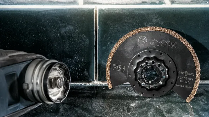 Een cirkelvormig hardmetalen zaagblad ligt op een betegelde ondergrond naast een elektrisch gereedschap.