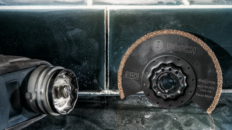 Een cirkelvormig hardmetalen zaagblad ligt op een betegelde ondergrond naast een elektrisch gereedschap.