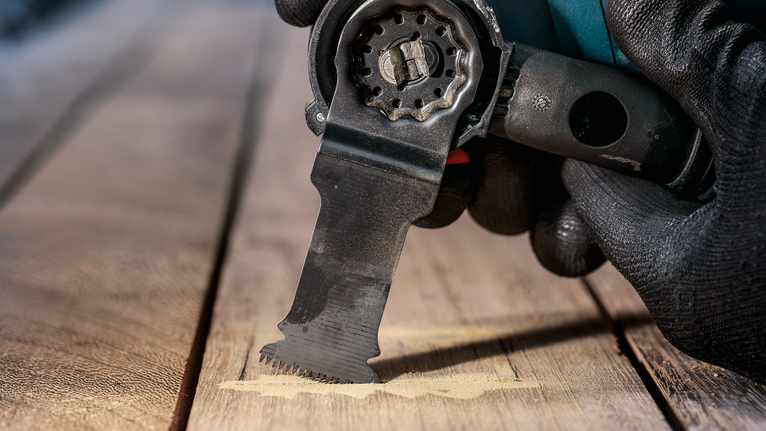 Een persoon die veiligheidsuitrusting draagt en een multitool gebruikt om hout te zagen.