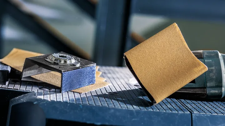 Detailschuurmachine met schuurpapier op een werkbank.