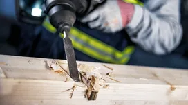Een persoon die veiligheidsuitrusting draagt, beitelt hout met een elektrisch gereedschap.