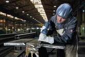 Een persoon die veiligheidsuitrusting draagt, gebruikt een rechte slijper op een metalen balk.