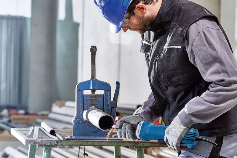 Een persoon die veiligheidsuitrusting draagt, gebruikt een rechte slijper om aan een metalen pijp te werken.