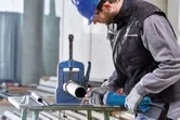 Een persoon die veiligheidsuitrusting draagt, gebruikt een rechte slijper om aan een metalen pijp te werken.