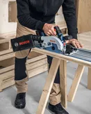 Een persoon met veiligheidsuitrusting zaagt hout met een cirkelzaag op een werkbank.