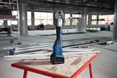 Snoerloze pers op een werkbank, omringd door metalen buizen op een bouwplaats.