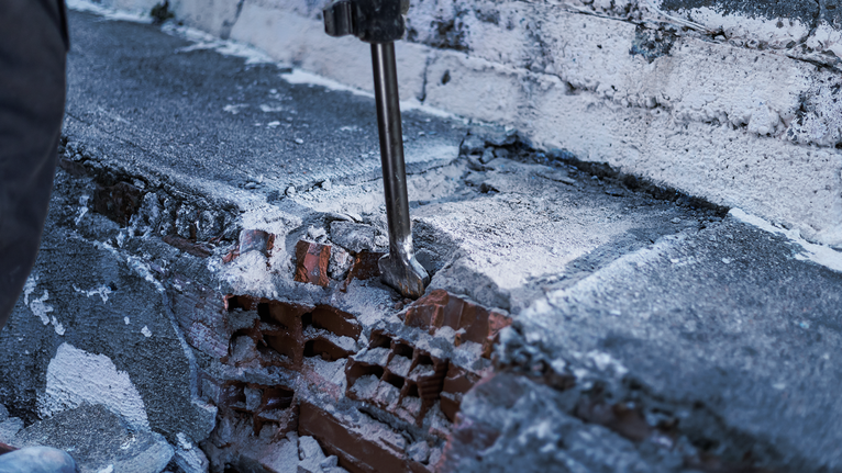 Sloopgereedschap breekt beton op een bakstenen muur.