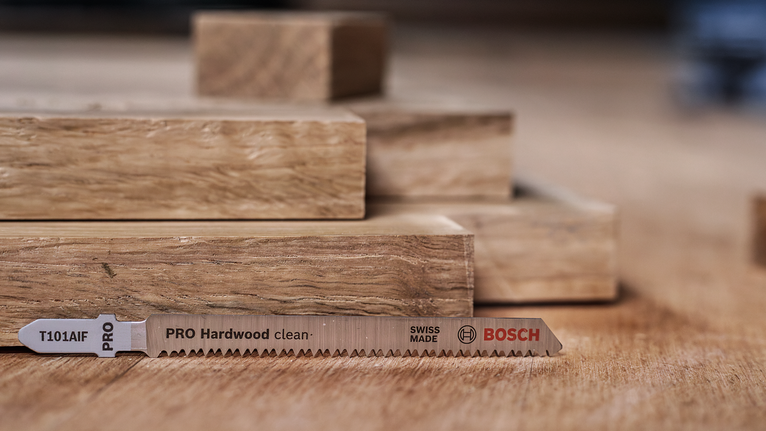 Een zaagblad ligt op een houten oppervlak naast gestapelde houten planken.