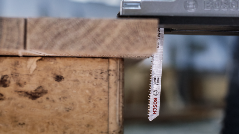 Een decoupeerzaag zaagt door een houten plank in een werkplaats.