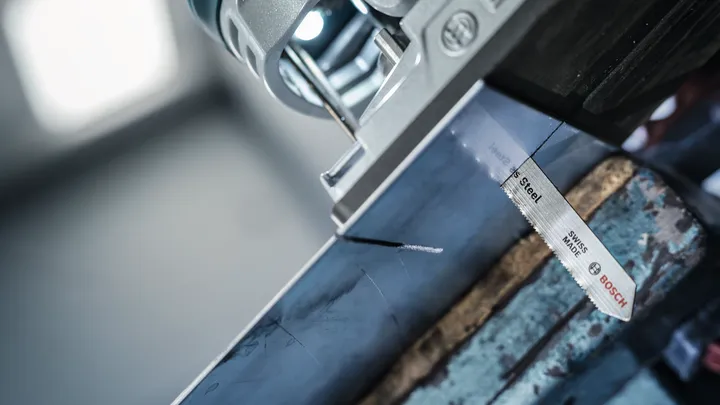 Een decoupeerzaag zaagt door een gemarkeerde metalen balk in een werkplaats.