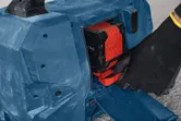Een persoon die veiligheidsmateriaal draagt, plaatst een batterij in een blauwe bouwplaatsradio.