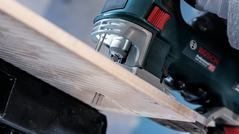 Persoon gebruikt een decoupeerzaag om door een houten plank te zagen.