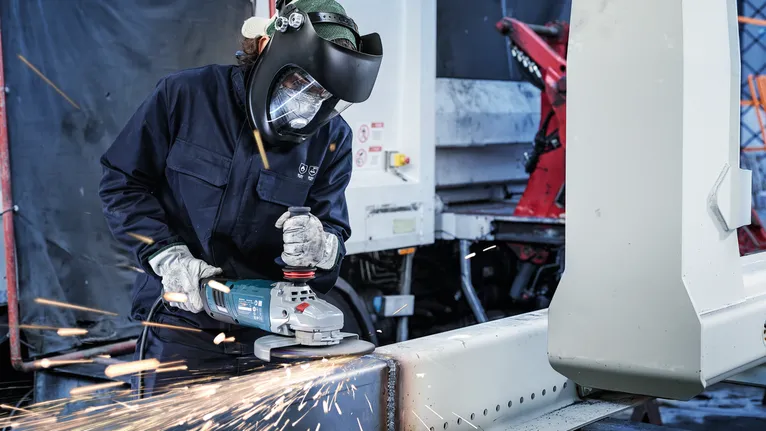 Een persoon die veiligheidsuitrusting draagt, schuurt tegen een metalen balk, waardoor vonken ontstaan.