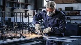 Een arbeider met veiligheidsuitrusting slijpt metaal, waardoor vonken ontstaan in een fabriek.