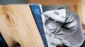 Persoon die veiligheidsuitrusting draagt en een houten oppervlak schuurt.