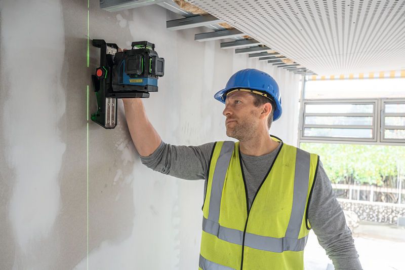 Een persoon met veiligheidsuitrusting richt een laserwaterpas op een muur.