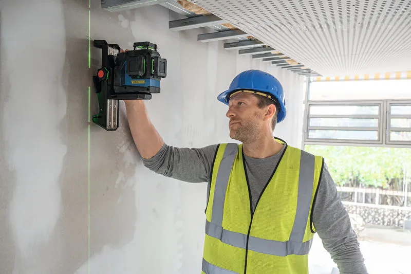 Een persoon met veiligheidsuitrusting richt een laserwaterpas op een muur.