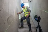 Een persoon met veiligheidsuitrusting markeert met een laserwaterpas een muur op de trap.