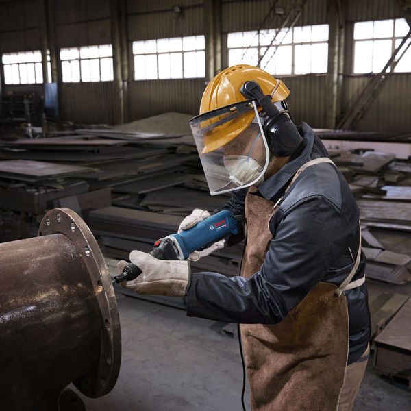 Een persoon die veiligheidsuitrusting draagt, slijpt een metalen pijpflens met een rechte slijper.