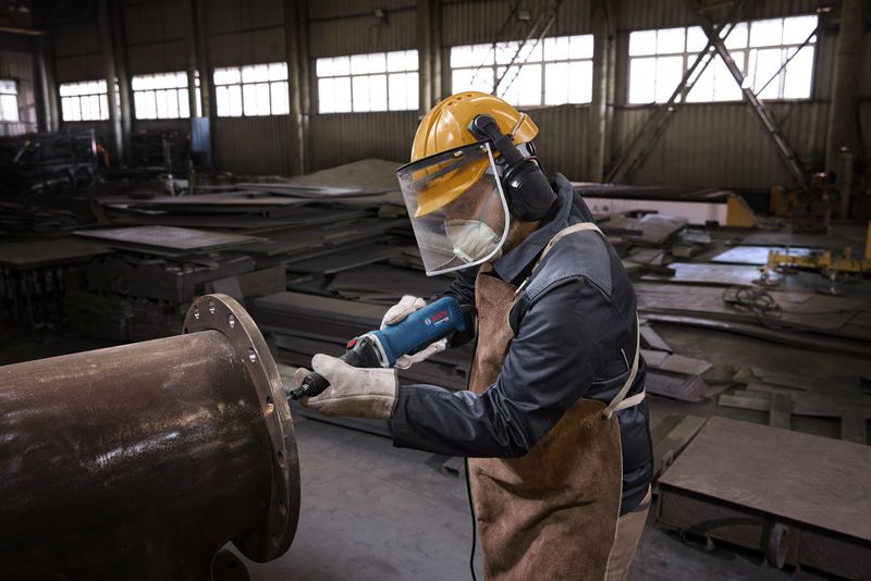Een persoon die veiligheidsuitrusting draagt, gebruikt een rechte slijper om aan een grote metalen pijp te werken.