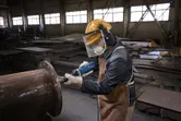Een persoon die veiligheidsuitrusting draagt, gebruikt een rechte slijper om aan een grote metalen pijp te werken.