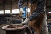 Een persoon die veiligheidsuitrusting draagt, slijpt metaal met een rechte slijpsteen, waarbij vonken ontstaan.