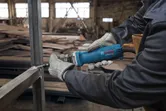 Een persoon met veiligheidsuitrusting slijpt een metalen frame met een rechte slijper.
