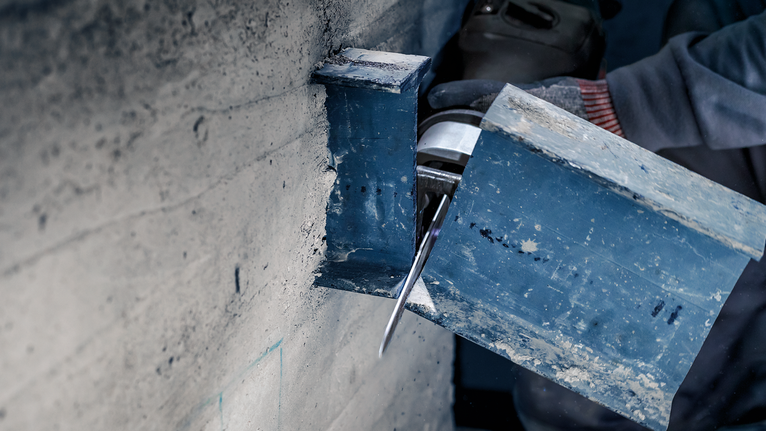 Een persoon met veiligheidsuitrusting zaagt met een elektrisch gereedschap door een stalen balk.