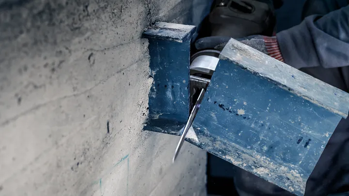 Een persoon met veiligheidsuitrusting zaagt een metalen balk door met een elektrisch gereedschap.