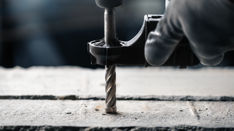Een persoon die veiligheidsmateriaal draagt, boort met een boormachine een gat in beton.