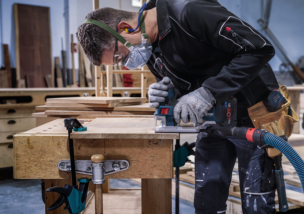 Een persoon die veiligheidsuitrusting draagt, gebruikt een elektrisch gereedschap om hout te zagen op een werkbank.