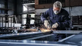 Een persoon die veiligheidsuitrusting draagt, slijpt metaal en veroorzaakt vonken in een industriële werkplaats.