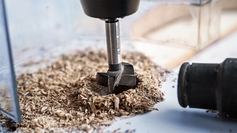 Boor die een gat in hout maakt, omgeven door houtsnippers.
