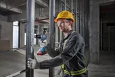 Een persoon die veiligheidsuitrusting draagt, gebruikt een accuboormachine op een metalen frame.