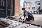 Een persoon die veiligheidsuitrusting draagt, gebruikt een accuboormachine om buiten vlonderplanken te installeren.