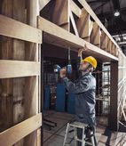 Een persoon die veiligheidsuitrusting draagt, boort in een houten balk terwijl hij op een ladder staat.