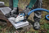 Een persoon met veiligheidsuitrusting slijpt beton door met een grote haakse slijper die is aangesloten op een stofzuiger.