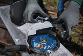 Een persoon met veiligheidsuitrusting stelt een grote haakse slijper met stofafzuiging af.