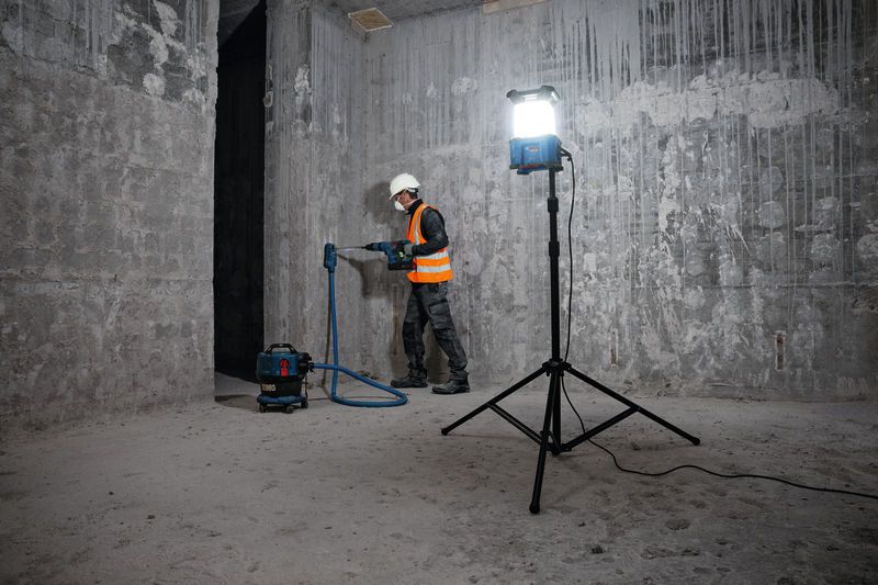Een persoon met veiligheidsuitrusting boort in een betonnen muur op een bouwterrein.
