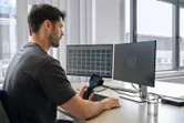 Een persoon analyseert warmtebeelden op twee beeldschermen met behulp van een warmtebeeldcamera aan een bureau.