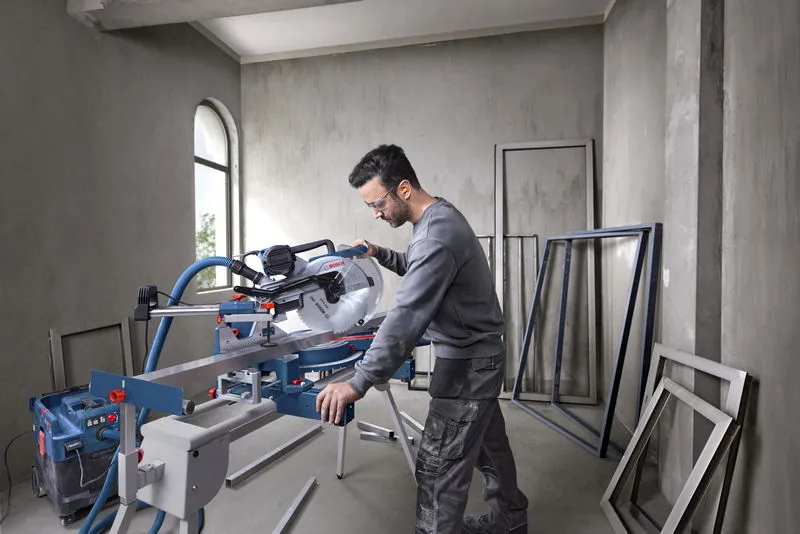Een persoon die veiligheidsuitrusting draagt, bedient een verstekzaag om binnenshuis metalen frames te zagen.