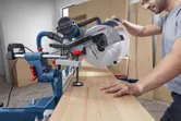 Iemand bedient een verstekzaag om een houten plank te zagen in een werkplaats.