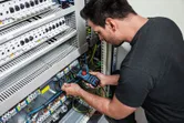 Een persoon test elektrische draden in een bedieningspaneel met behulp van een vorkmeter.
