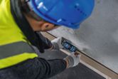 Persoon die veiligheidsuitrusting draagt, meet de afstand tot de muur met een lasermeter.