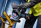 Een persoon met veiligheidsuitrusting zaagt een metalen pijp door met behulp van een snoerloze haakse slijper.