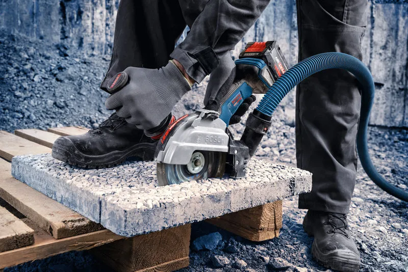 Een persoon met veiligheidsuitrusting zaagt een betonplaat door met een snoerloze haakse slijper.