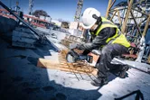 Een persoon met veiligheidsuitrusting zaagt op een bouwplaats betonijzer door met een snoerloze haakse slijper.