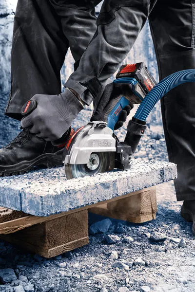 Een persoon met veiligheidsuitrusting zaagt beton met een snoerloze haakse slijper.
